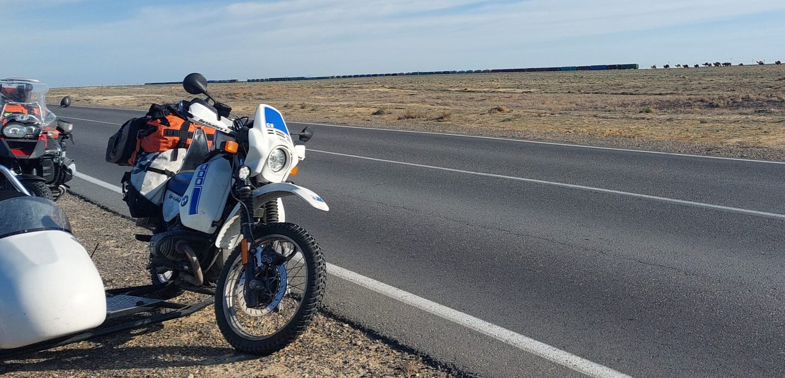 Roadside in the Kazakh steppe: a freight train, camels, and the R80 with sidecar — 9 April 2026